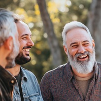 Group of men laughing and enjoying a genuine conversation outdoors, dressed casually, expressions of openness and camaraderie, celebrating positive masculinity and supportive friendship