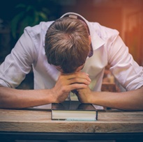 The young man handsome caucasian Americans handsome man sitting with hands clasped in prayer for blessings from God. A Bible rested on a wooden table with copy space