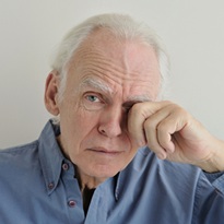 Portrait of a gray-haired elderly crying man wiping away his tears with his hand